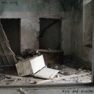 A room in an abandoned house scattered with debris including an open refrigerator lying on its side and bits of broken wood.